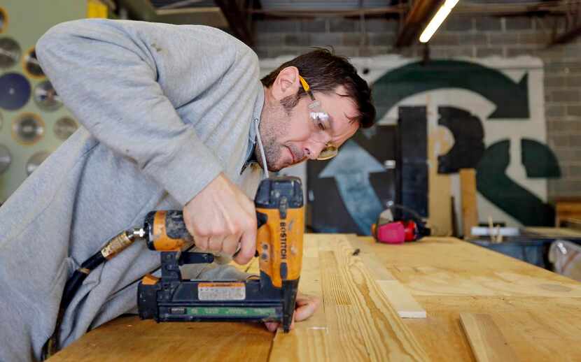 
Kevin Rennels uses a compressed air stapler to secure wood planks, from recycled and...