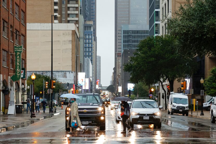 Pedestrians take shelter from the rain under umbrellas while crossing a rainy Elm Street at...