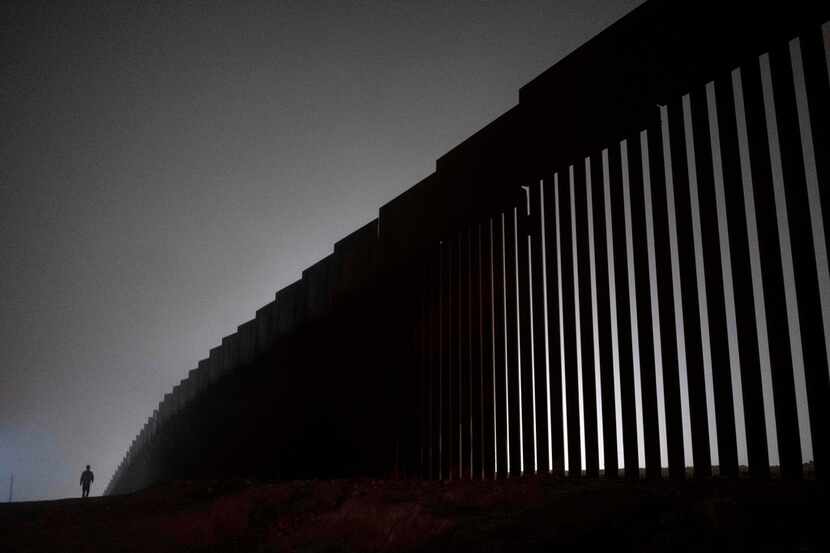 A man walks next to a reinforced section of the US-Mexico border fence is seen from Tijuana,...