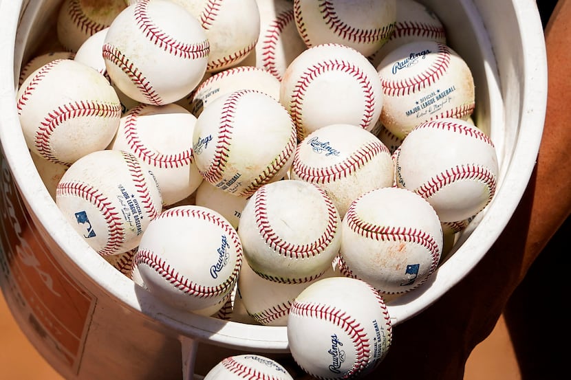 Texas Rangers infielder Greg Bird dumps a bucket of baseballs from infield practice into a...