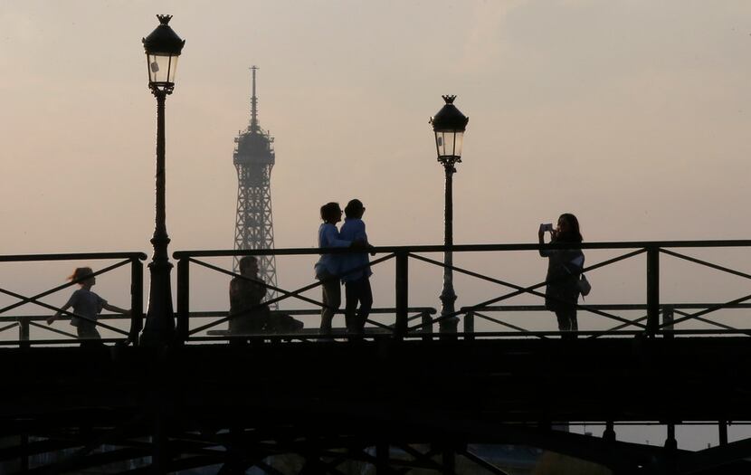 People enjoy the sunset as they cross the Pont des Arts in Paris, France. Eiffel Tower in...
