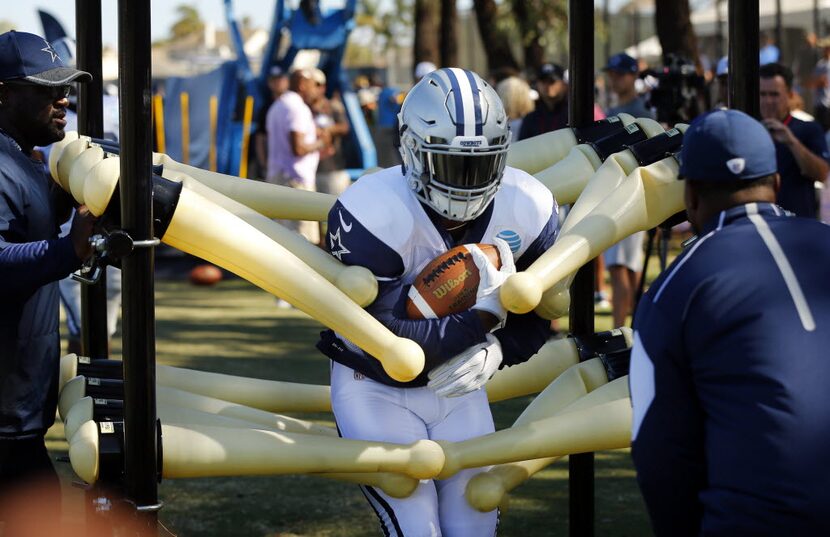 Dallas Cowboys running back Ezekiel Elliott (21) runs through a tackling machine during...