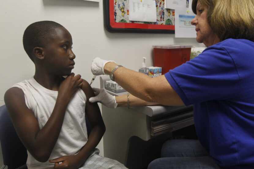 Corey Brooks, 11, gets one of four immunizations from registered  nurse Kathy Collar at the...