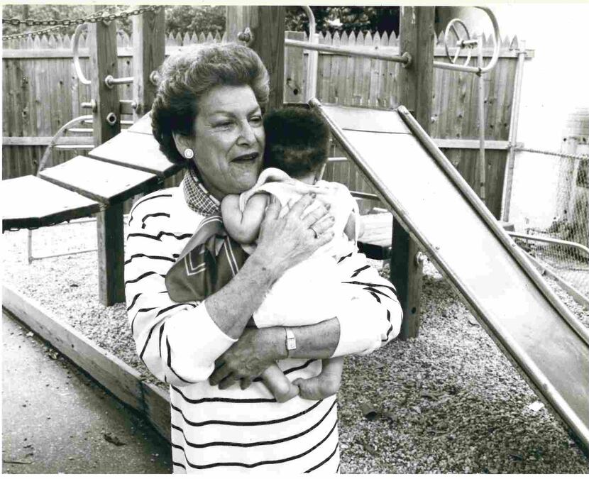 A black and white photo of The Family Place founder Gerry Beer holding a baby at a playground.