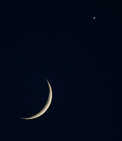  The crescent moon appears alongside the planet Venus in the western sky as seen from...