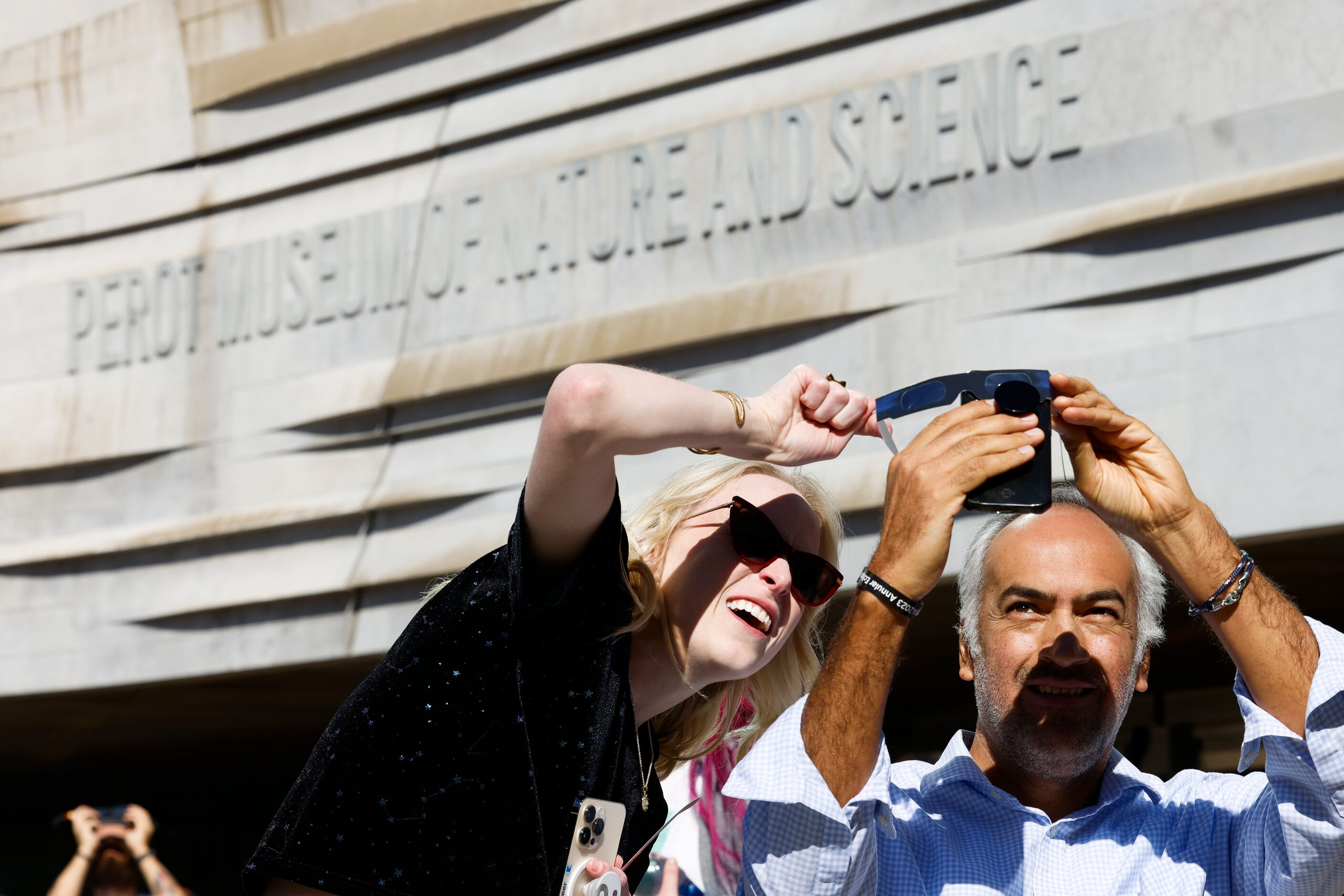 Kittie Greer of Dallas (left) helps Alejandro Olivo with taking a photo of the annular solar...