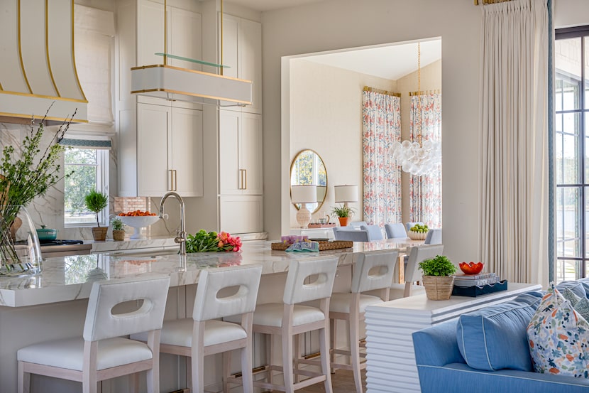 White kitchen with brass trim, with white pleather seats at the island adjacent to a blue sofa