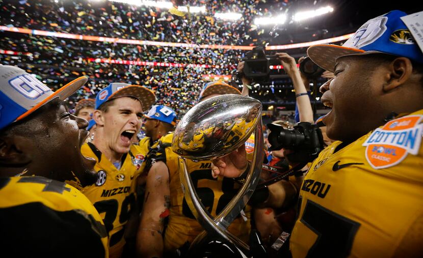 the Missouri Tigers football players celebrate with the winning trophy after defeating the...