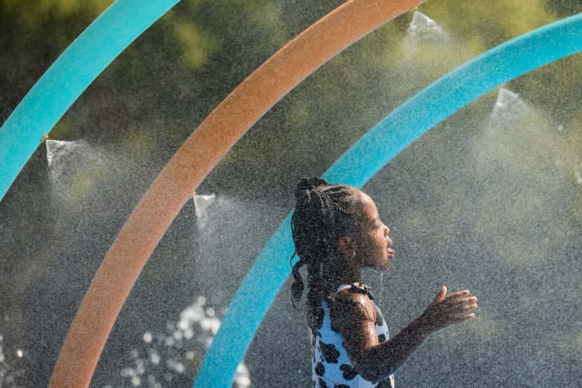 Alivia Hicks, 4, cools off from the July heat at the Old Town Splash Pad behind Wayne Frady...