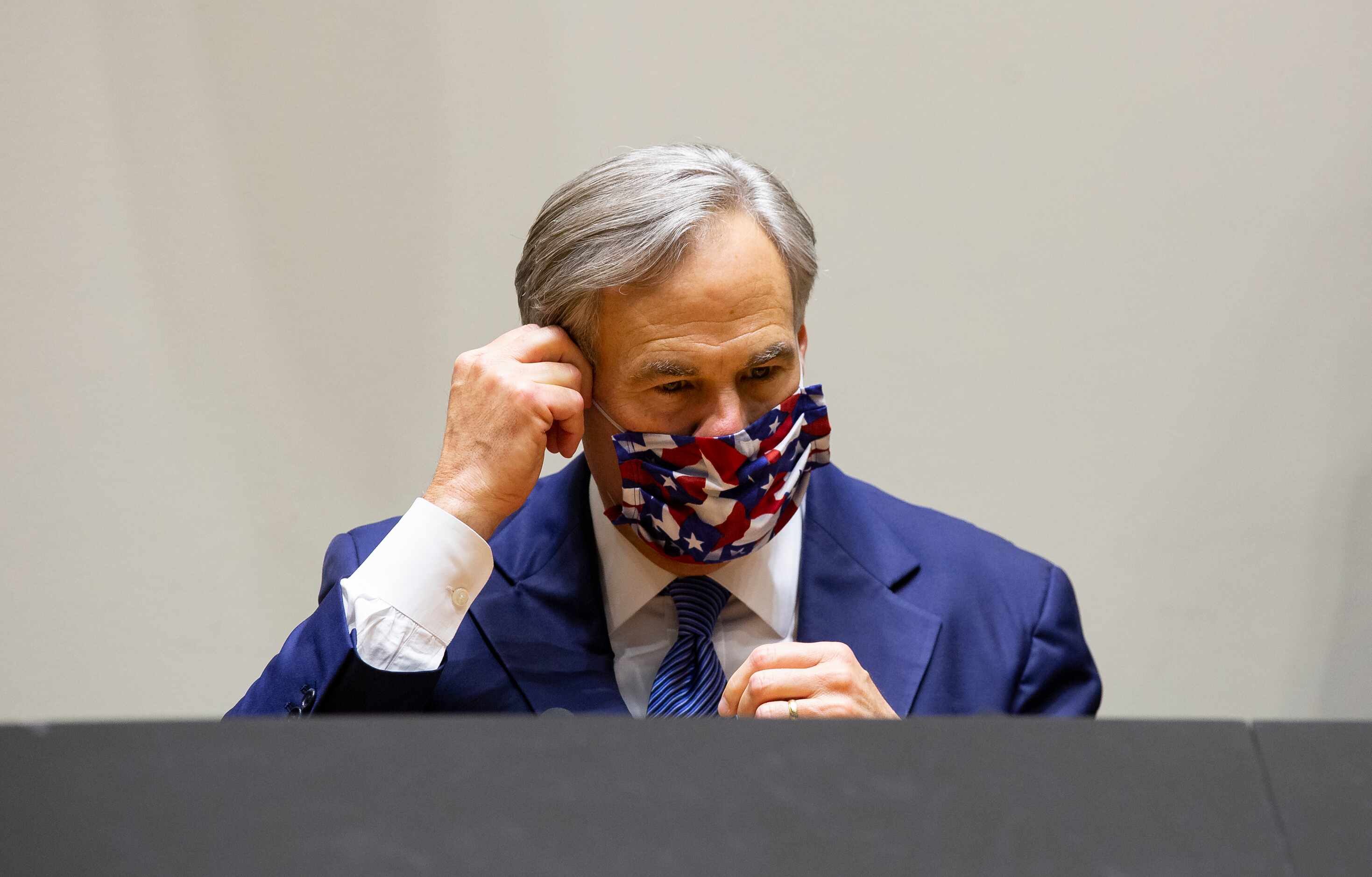 Governor Greg Abbott takes off his mask before speaking at a press conference on protest...