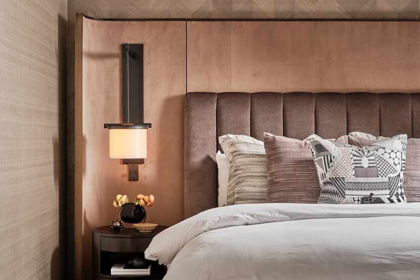 Next to an upholstered bed, a decorative sconce is mounted above a bedside table and lends a...