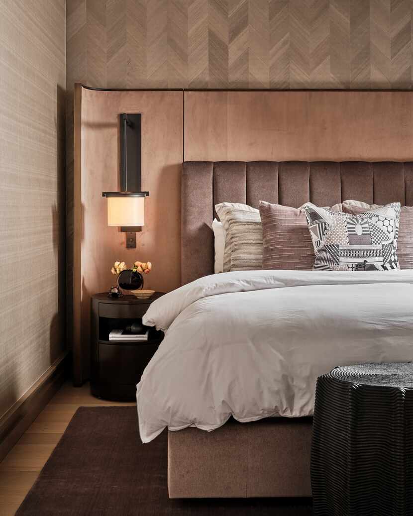 Next to an upholstered bed, a decorative sconce is mounted above a bedside table and lends a...