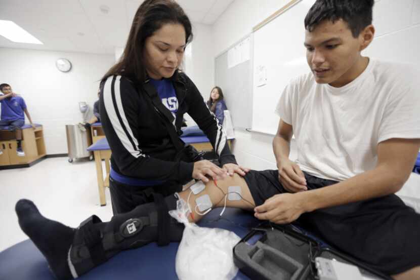 Athletic trainer Amy Perez applies electrodes to senior running back Julian Baeza's right...