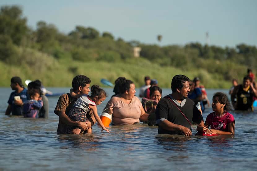 Migrants navigate around concertina wire along the banks of the Rio Grande after crossing...