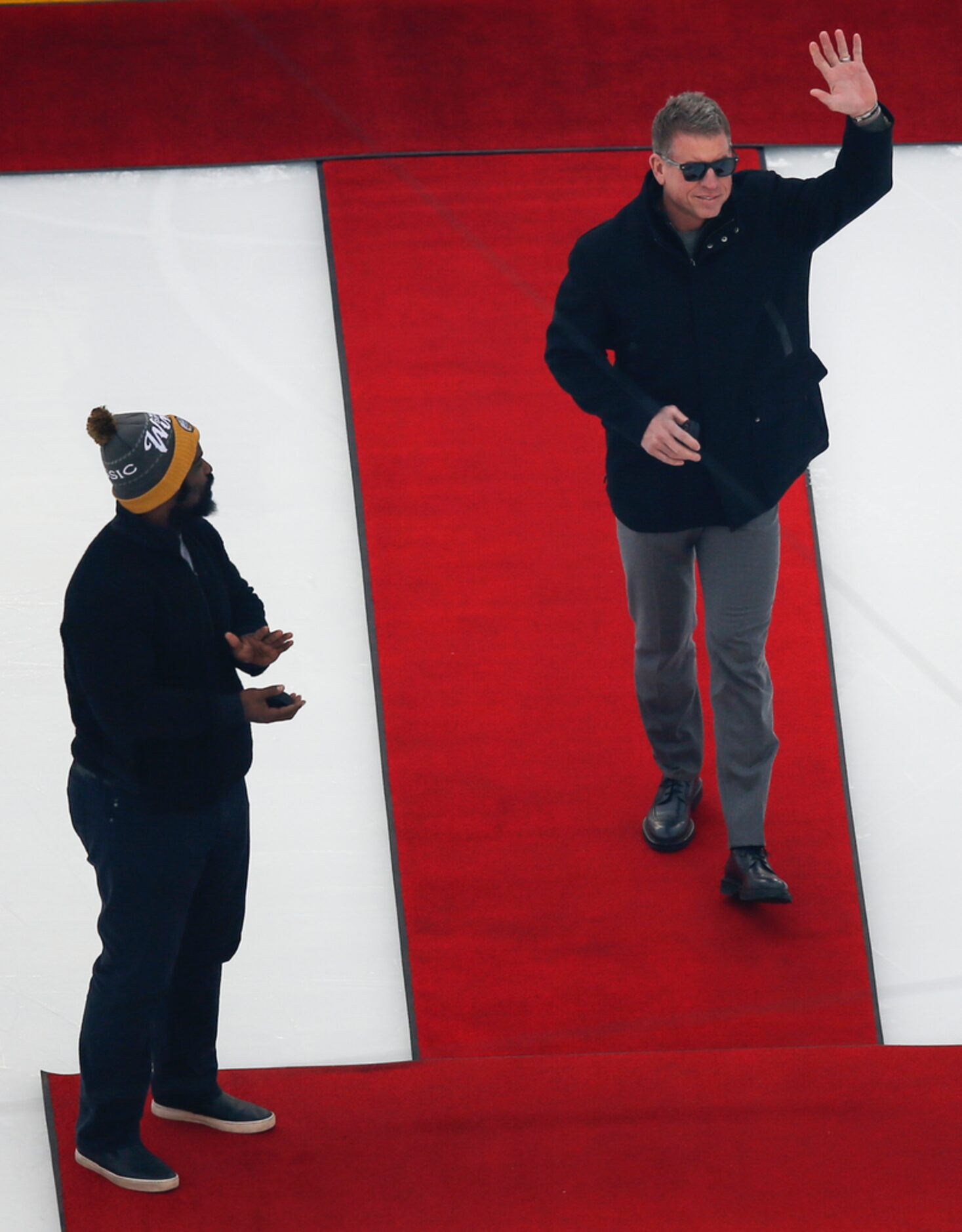 Troy Aikman, right, joins Ricky Williams, left, on the ice to participate in the puck drop...