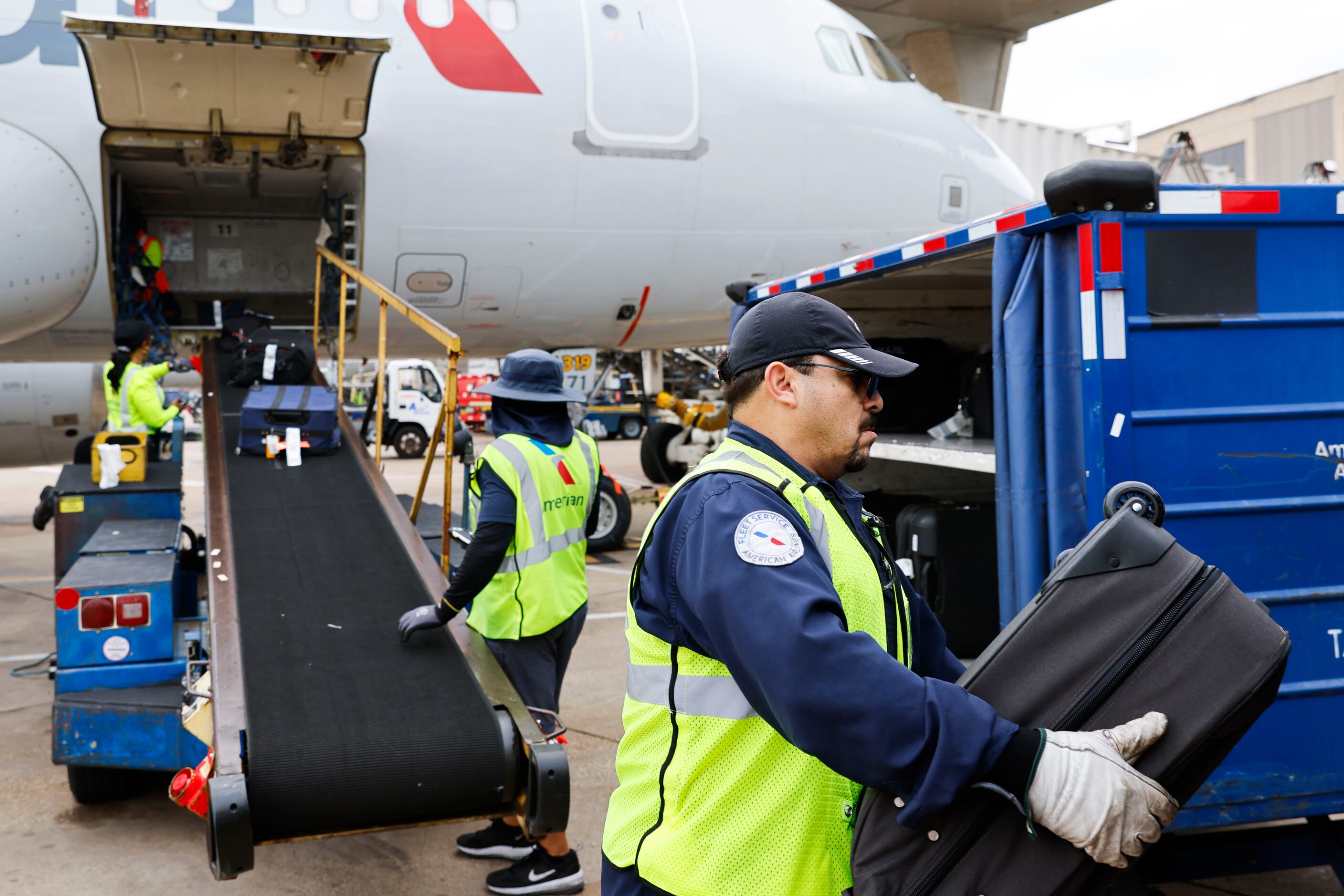 Members of the ground crew unload baggages from an American Airlines flight from Grand...