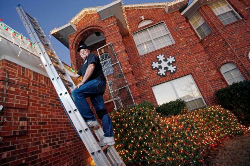 Bob Adams stands on a ladder while organizing Christmas light decorations outside his home...