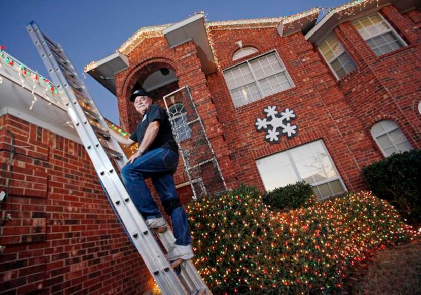 Bob Adams stands on a ladder while organizing Christmas light decorations outside his home...