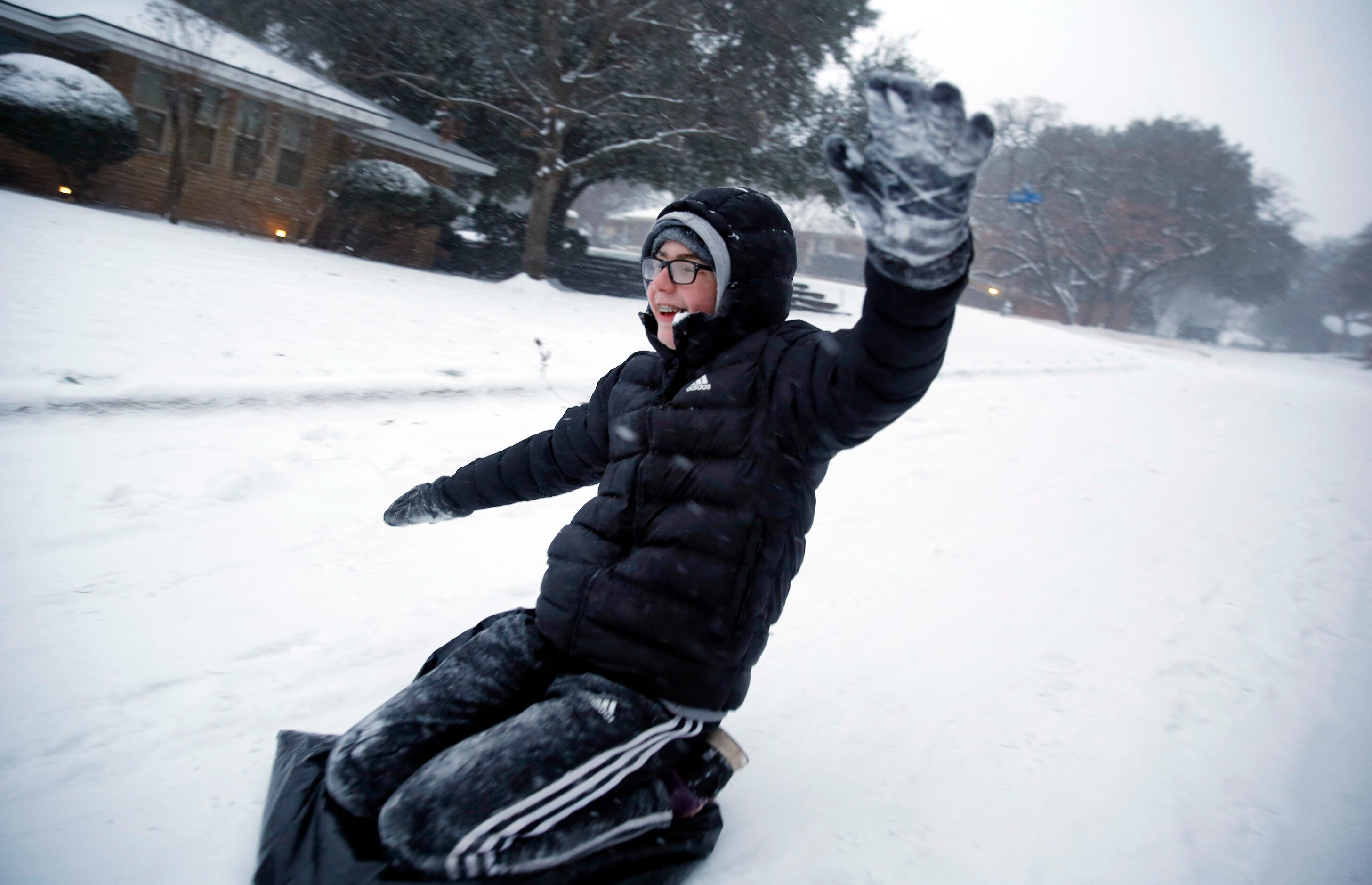 Jonathan Lewis uses a black plastic bag to sled down a steep, snow-covered street in North...