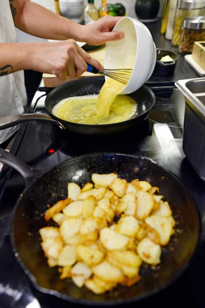 Chef Angela Hernandez pours scrambled egg into a pan as she prepares a dish of potato with...