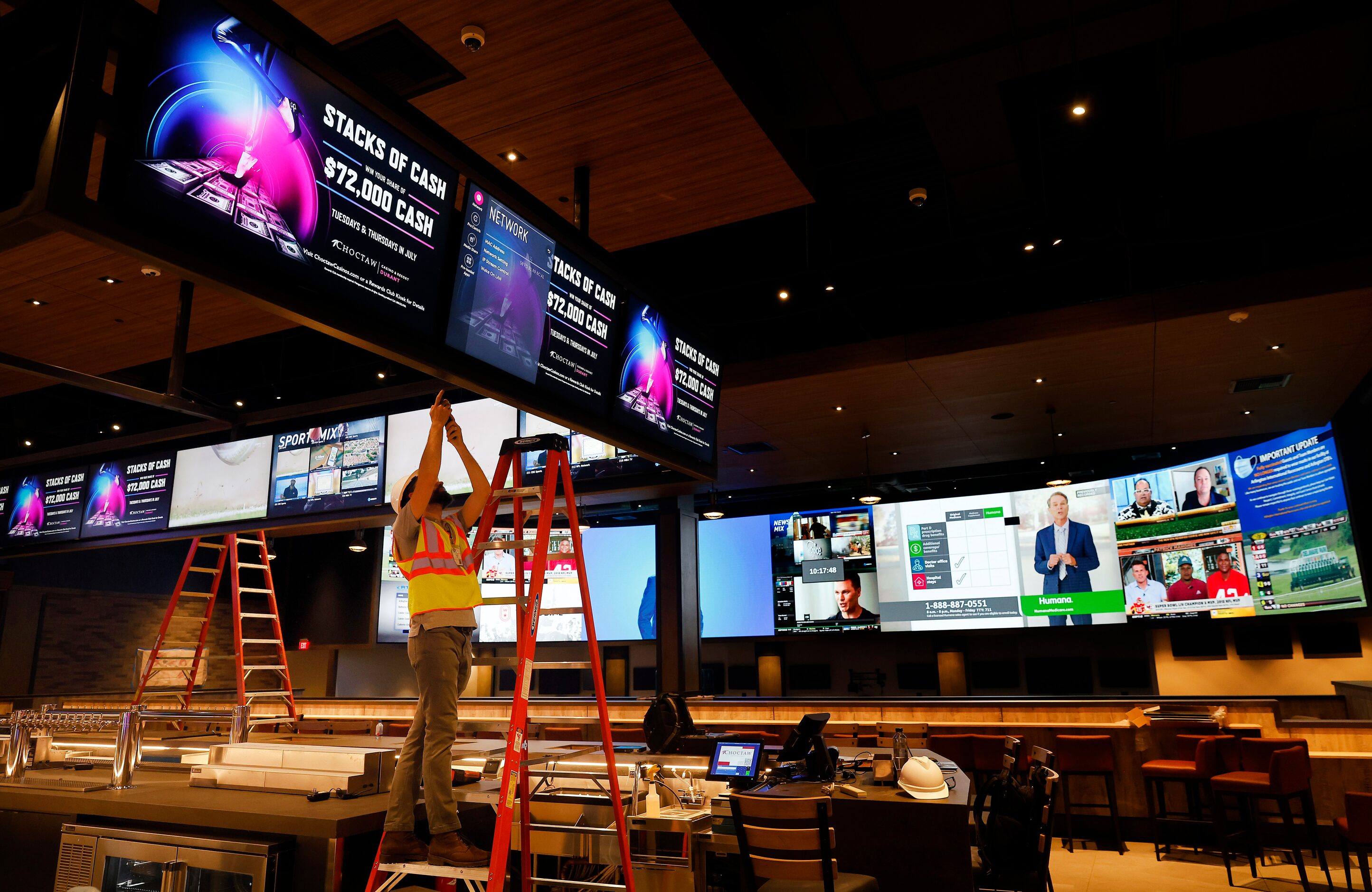 A worker puts the finishing touches on a bank of video screens hanging over The League...