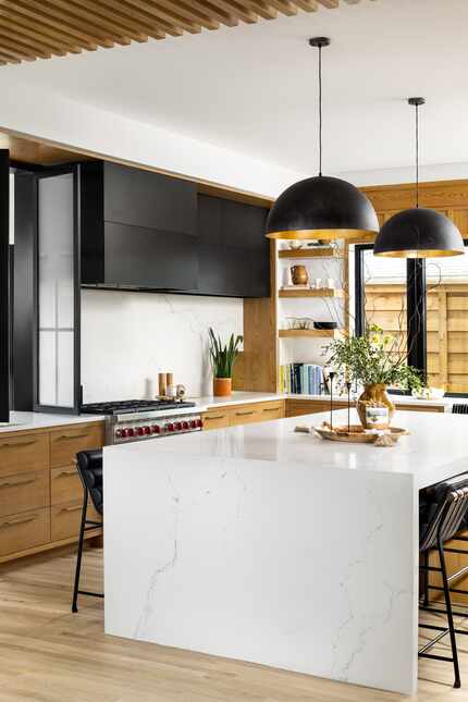 Modern kitchen with large quartz island, black floating cabinets and light brown wooden...