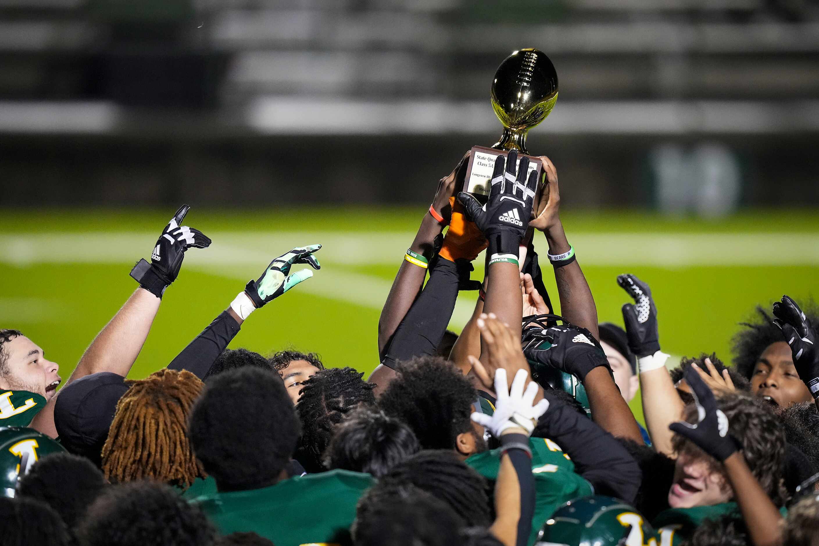 Longview players celebrate with the game trophy after a victory over Mansfield Timberview in...