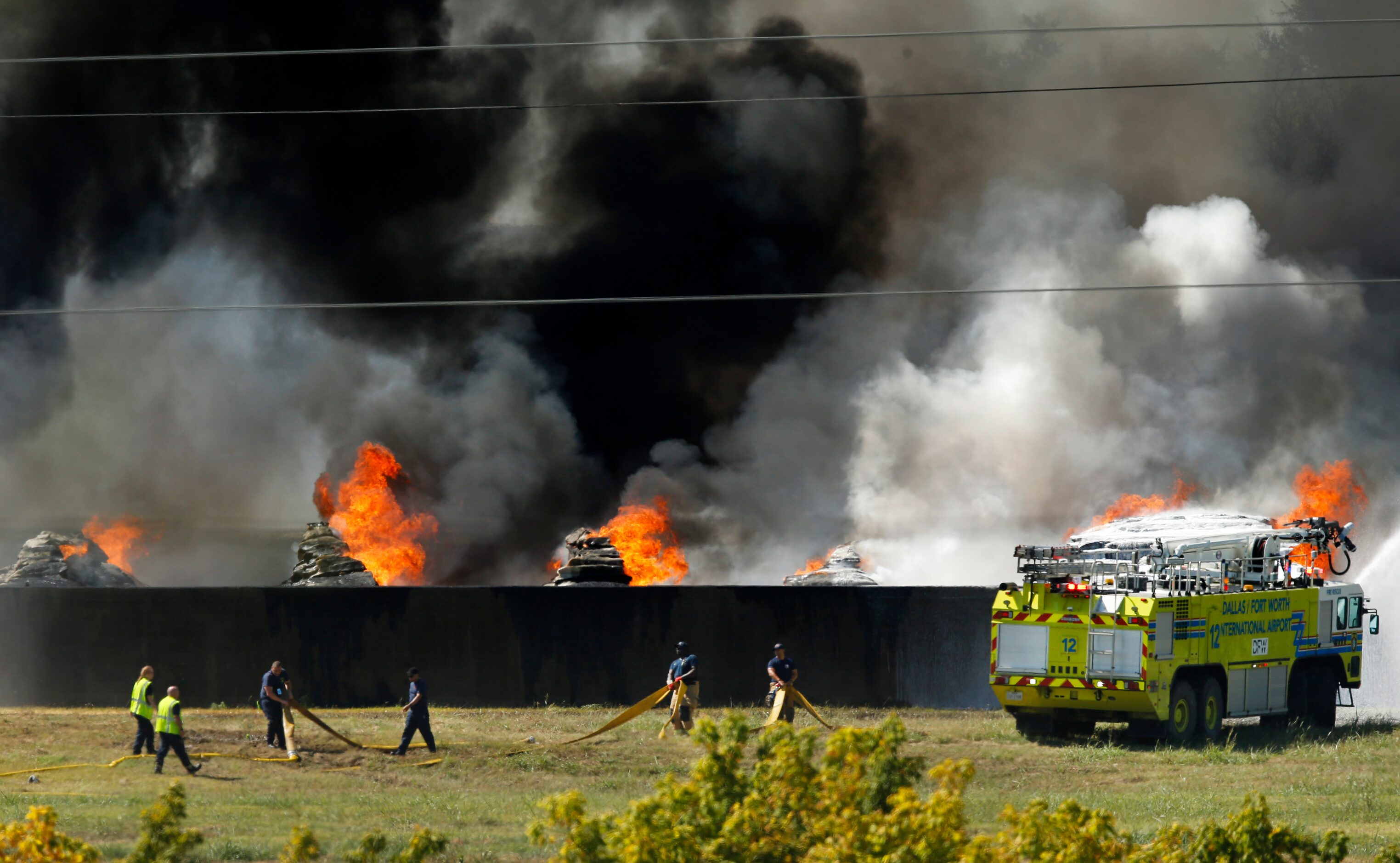 Firefighters drag hose as a DFW International Airport fire truck douses burning plastic at...