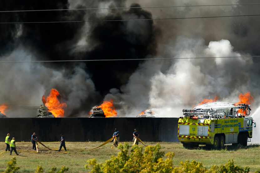 Firefighters drag hose as a DFW International Airport fire truck douses burning plastic at...