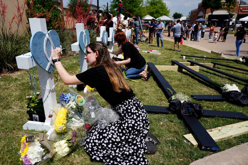 Jennifer Seeley signs a cross that stands by others at a makeshift memorial by the mall...