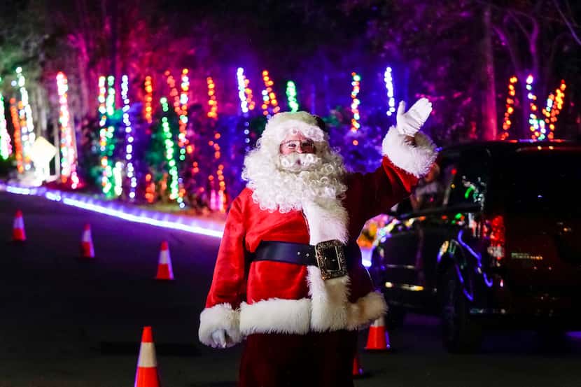 Santa waves to visitors passing in their cars during Dallas Zoo Lights on Wednesday, Nov....