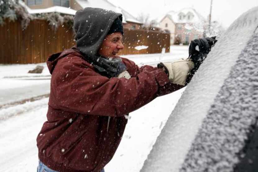 
Burt Starr scrapes ice off of his windshield in front of his house in Plano after the ice...