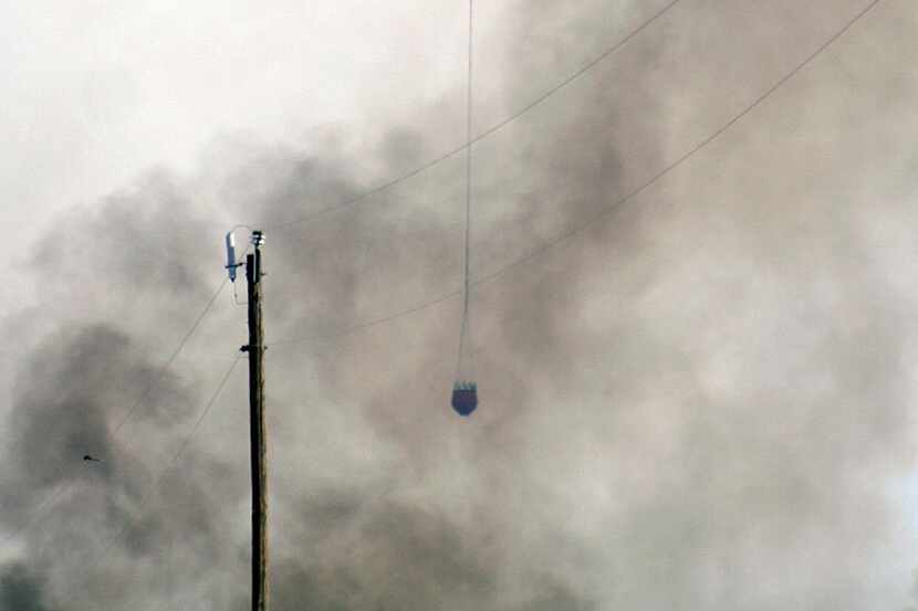 A helicopter moves in through smoke to drop water on a wildfire north of Woodward, Okla., on...