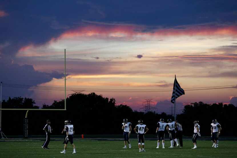 Jesuit players wait for the play to resume as the sun falls during a high school football...