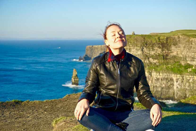 Lauren McGaughy meditates near the edge of the Cliffs of Moher, with O'Brien's Tower off in...