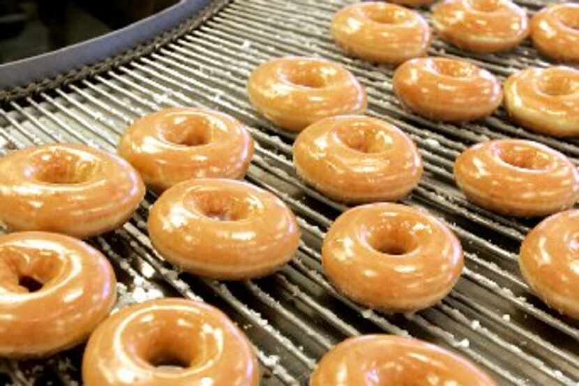 Freshly iced doughnuts roll by on a conveyor belt at the Krispy Kreme store in...