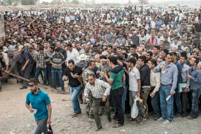 Hundreds of men, women and children wait to cross into Kurdish Iraq from territory ruled by...