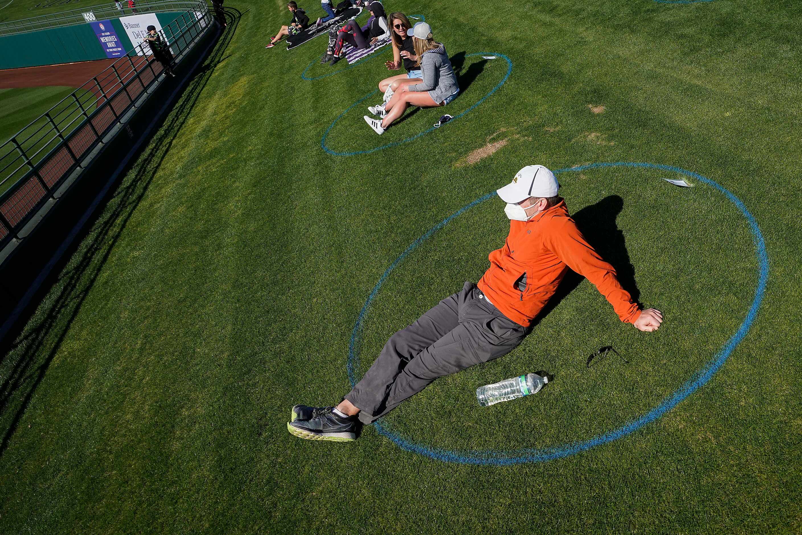 Fans watch from social distancing circles painted on the outfield lawn during a spring...