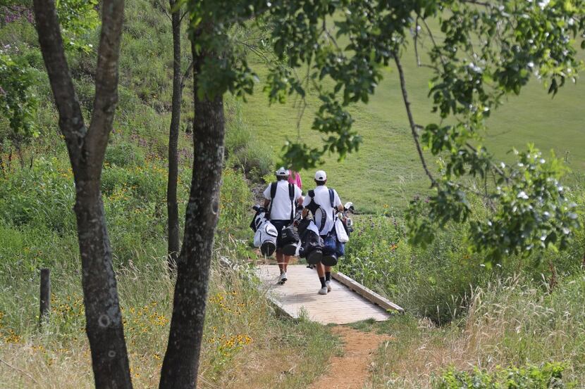 Caddies carry clubs for players along the course during a tour of the Trinity Forest Golf...