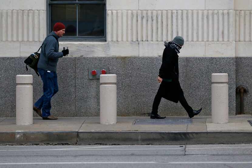 People walk down Houston St. as temperatures drop to the 20's in downtown Dallas on January...