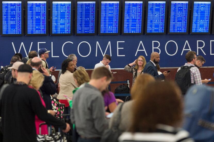 Passengers wait in line to check luggage as flight schedules are projected on screens in...