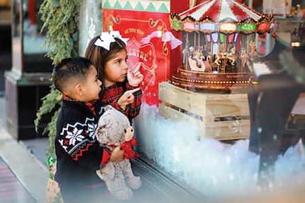 A little boy and little girl look at a store window's display of old-fashioned Christmas...