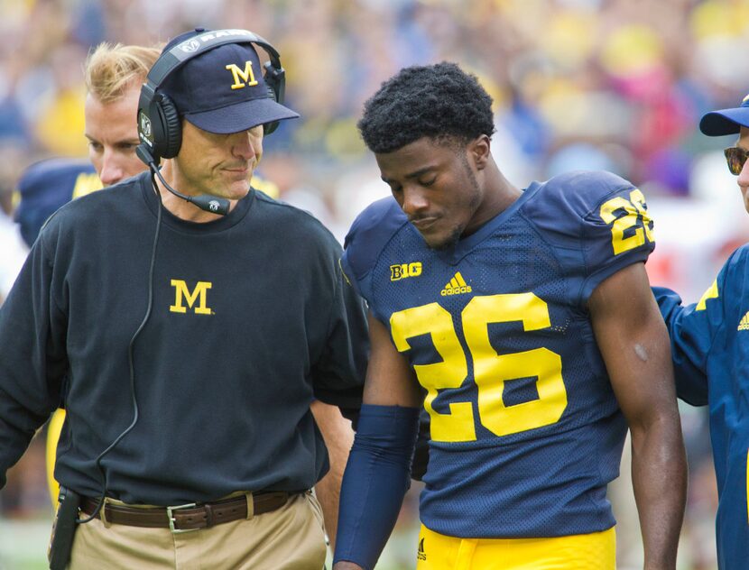 Michigan head coach Jim Harbaugh, left, escorts defensive back Jourdan Lewis (26) off the...