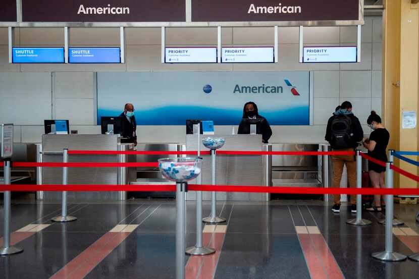 American Airlines employees check in two passengers at a mostly empty check-in counter in...