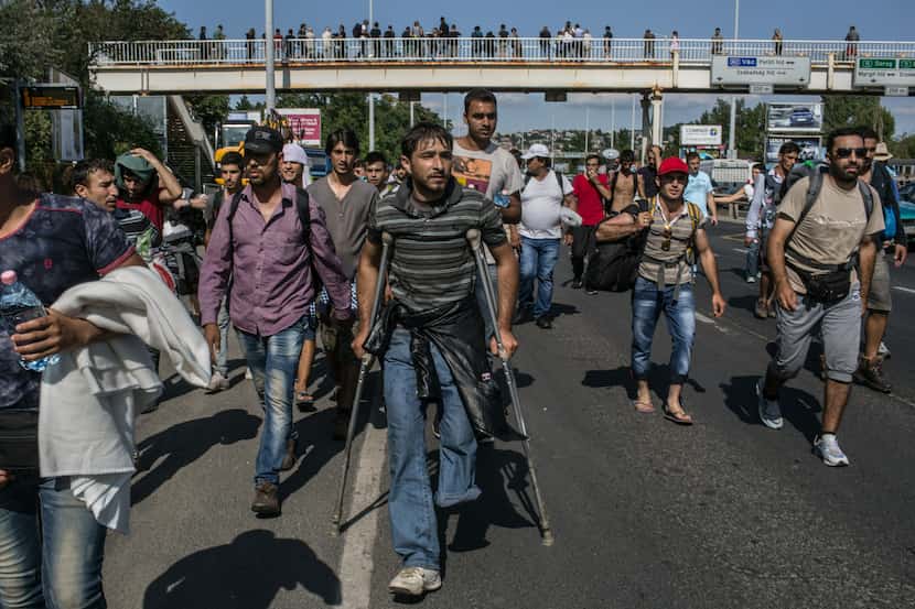 An amputee walks among a large group of migrants, many from Syria, in Hungary as they try to...