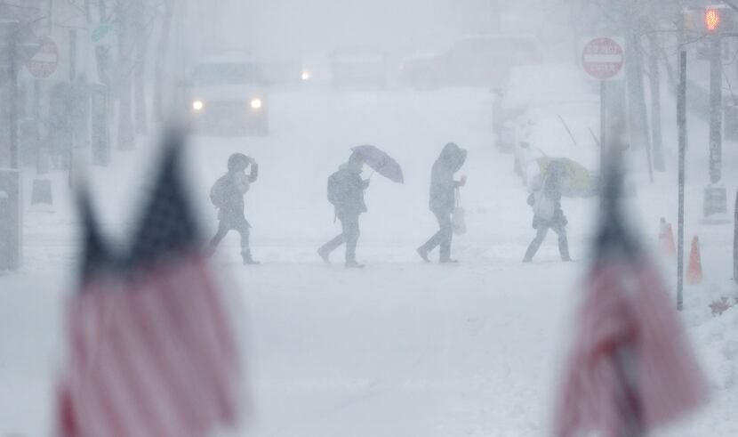 People walk across a snow-covered intersection behind American flags in Hoboken, N.J.,...