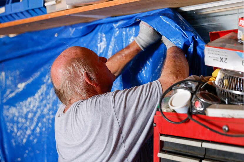 Burt Phillips staples a tarp to cover a window after it was blown out by an EF2 tornado...