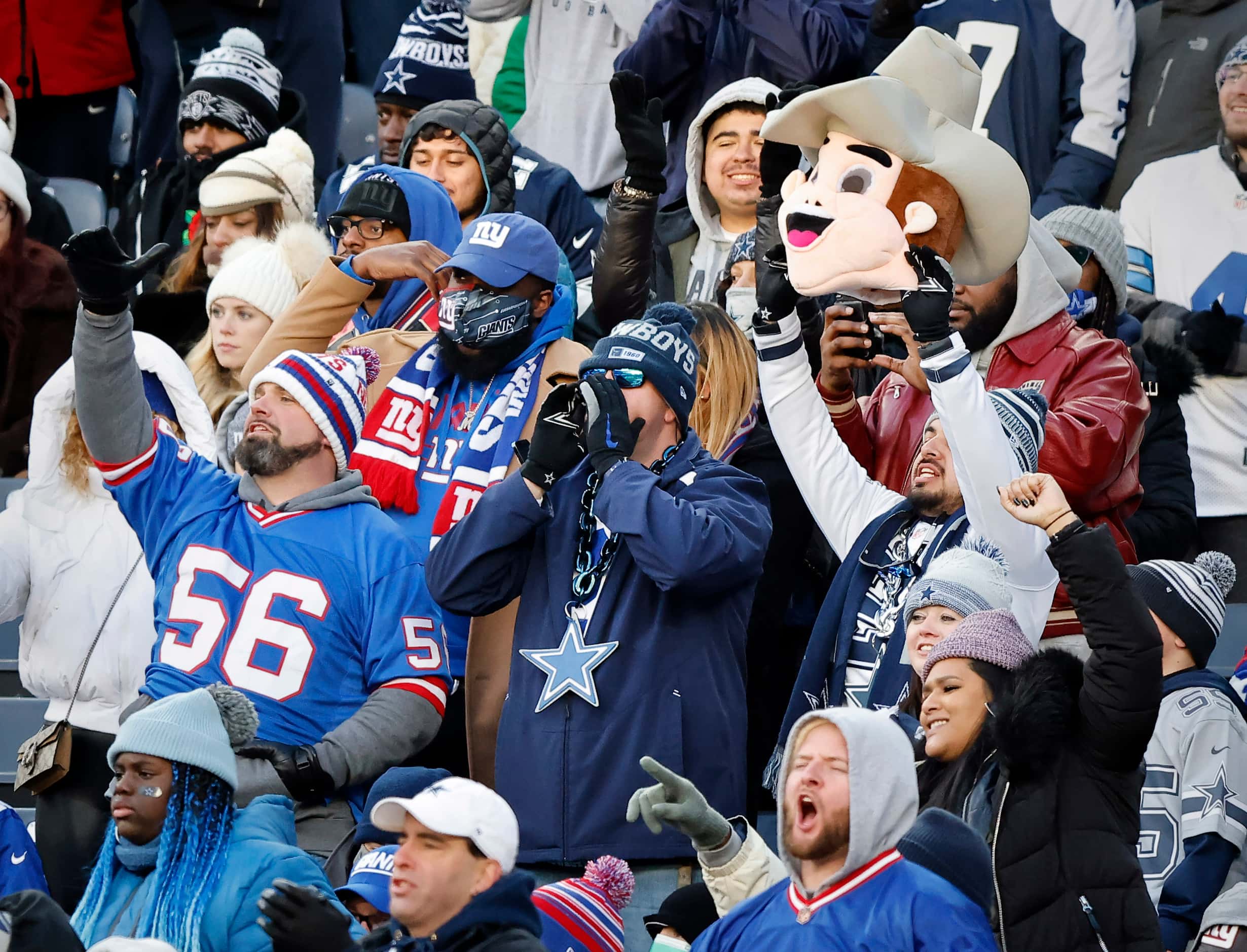 Dallas Cowboys fans, including one with a Rowdy mascot mask, cheer alongside New York Giants...