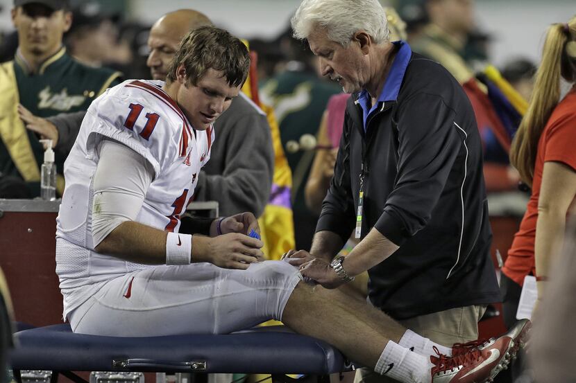 SMU quarterback Garrett Gilbert (11) is looked at by a trainer after injuring his leg during...