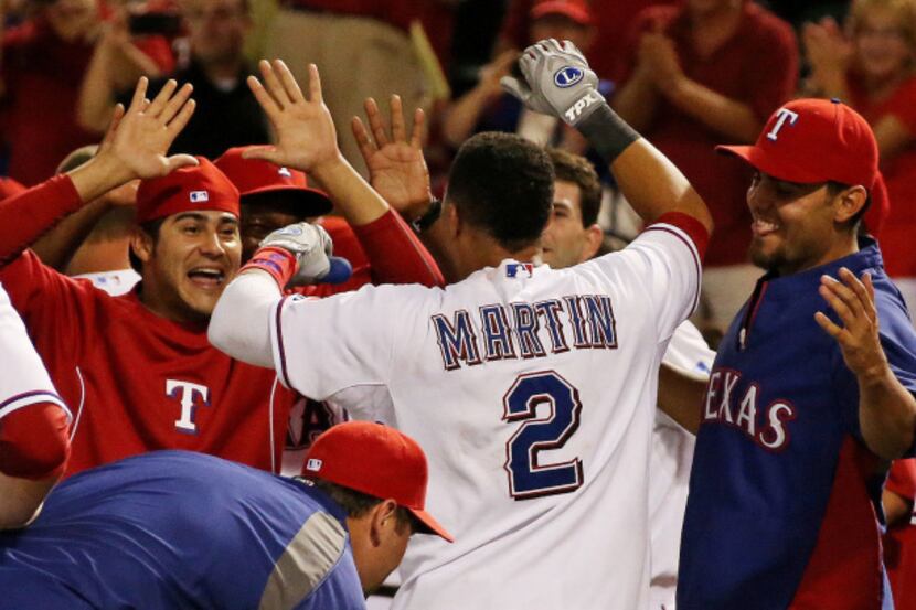 Texas' Leonys Martin is greeted by jubilant teammates at home plate  after hitting his...